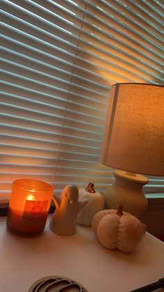 a table topped with a lamp next to a window covered in blinds and pumpkins