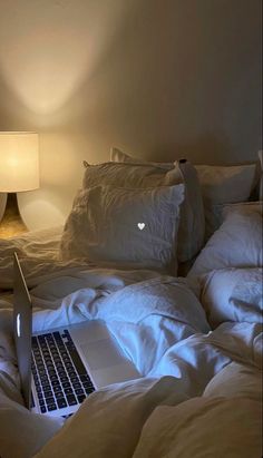 an open laptop computer sitting on top of a bed covered in white sheets and pillows