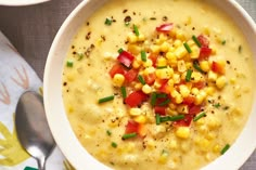 a white bowl filled with corn and garnish next to a spoon on top of a table