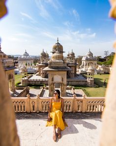 a woman in yellow dress sitting on the edge of a balcony looking out at an ornate building