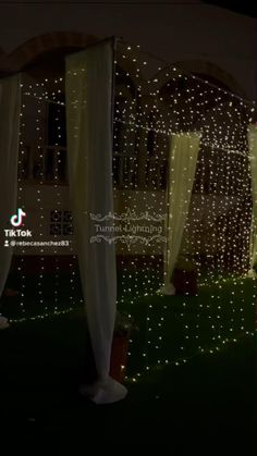 an outdoor gazebo decorated with white lights and draping on the grass at night