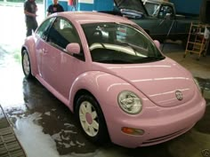 a pink car parked in a garage next to other cars and people standing around it