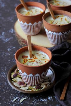 four cups filled with food sitting on top of a wooden plate next to spoons