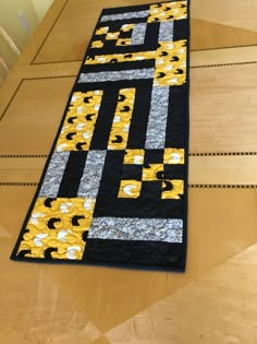 a quilted table runner with yellow and black squares on the top, sitting on a wooden floor