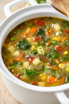 a white bowl filled with vegetable soup on top of a wooden table next to a spoon