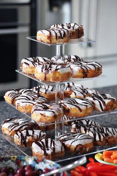 a stack of doughnuts with chocolate drizzled on them and fruit in the background