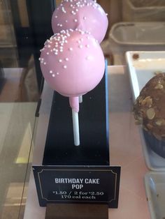 two pink cake pops sitting on top of a display case next to a muffin