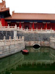 a small boat floating on top of a body of water next to a building with red walls