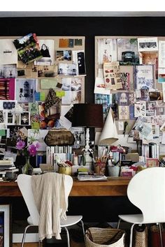 two white chairs sitting in front of a wooden desk covered with pictures and papers on the wall