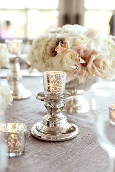 the centerpieces on this table are filled with white flowers and lit votive candles