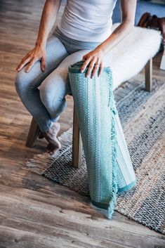 a woman is sitting on a chair with her legs crossed and holding a knitted blanket