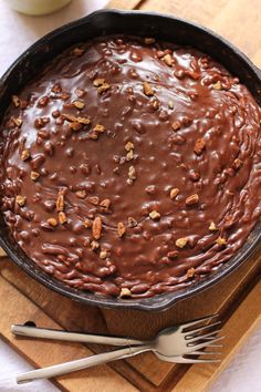 a chocolate cake in a pan with nuts on top and two forks next to it