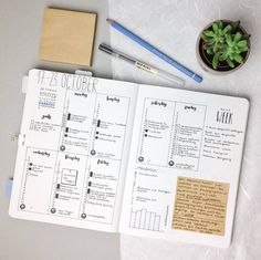 an open planner sitting on top of a table next to a plant and pencils