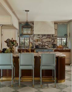 a kitchen with marble counter tops and blue chairs in front of an island that has gold trim