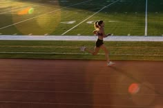 a woman running on a track with the sun behind her and grass in the background