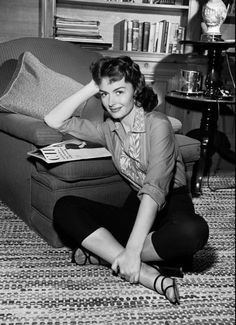 a black and white photo of a woman sitting on the floor next to a couch