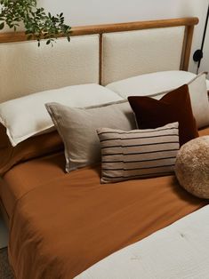 a bed topped with lots of pillows on top of it's headboard next to a potted plant