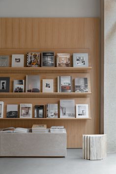 a book shelf filled with books next to a white stool and wall mounted shelving