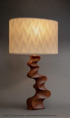 a wooden table lamp with a white shade on the top and an intricately carved wood base