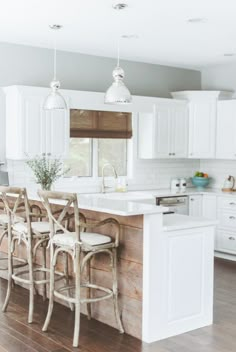 a kitchen with white cabinets and an island in the middle, surrounded by bar stools