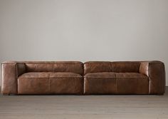 a brown leather couch sitting on top of a hard wood floor next to a wall