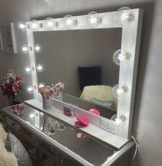 a vanity mirror with lights on top of it and a teddy bear sitting next to it