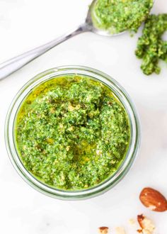 a small glass jar filled with pesto and almonds next to two spoons