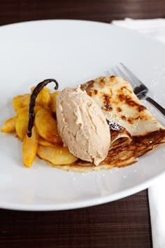 a white plate topped with food on top of a wooden table next to a knife and fork