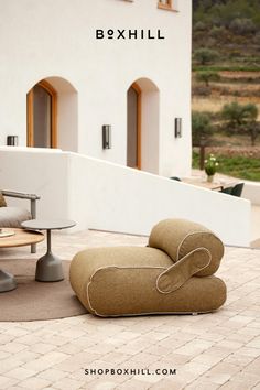 a chair and ottoman sitting on top of a brick floor next to a building with windows