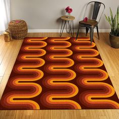 an orange and red rug in a living room with two chairs on the floor next to a potted plant