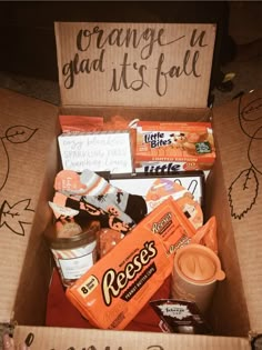 an open box filled with snacks and candy on top of a table next to a sign that says orange is glad it's fall