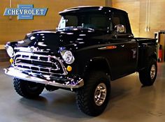 an old black pickup truck parked in a garage with the chevrolet logo on it's side