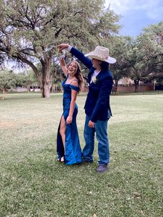 a man and woman standing in the grass with one holding up his arm to catch a frisbee