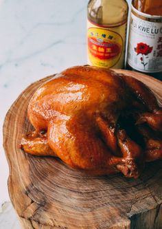 a whole chicken sitting on top of a wooden cutting board next to a bottle of beer