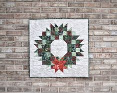 a quilted wall hanging on the side of a brick building with a green and red wreath