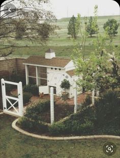 a small white house in the middle of a grassy area with trees and bushes around it