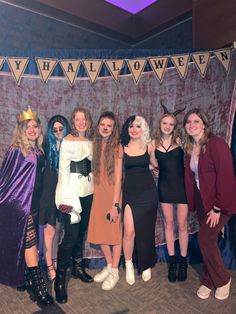 a group of women standing next to each other in front of a wall with halloween decorations