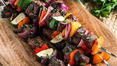 skewers of meat and vegetables on a wooden cutting board next to parsley