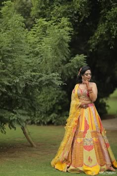 a woman in a yellow and red dress posing for the camera with trees behind her