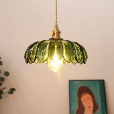 a green light hanging from a ceiling next to a painting on the wall and potted plant