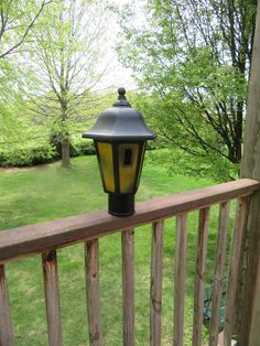 a black and yellow lamp on top of a wooden rail next to a green field