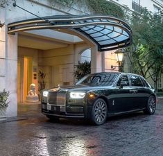 a black rolls royce parked in front of a hotel entrance with an awning over it