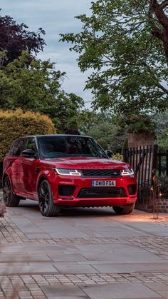 a red range rover is parked in front of a gate and some trees on the sidewalk