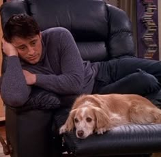 a man sitting in a recliner with his arm on the back of a dog