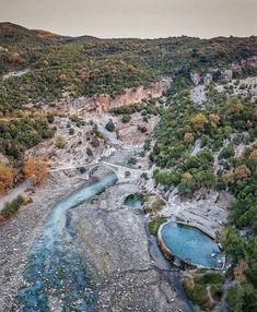 an aerial view of a river flowing through a valley surrounded by mountains and trees in the fall