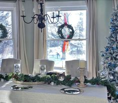 a dining room table decorated for christmas with wreaths on the windowsill and candles