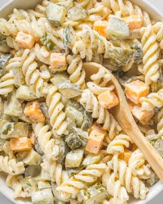 a bowl filled with pasta and vegetables next to a wooden spoon