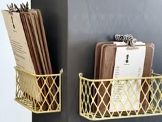 two metal baskets holding files and folders on the side of a gray wall next to each other