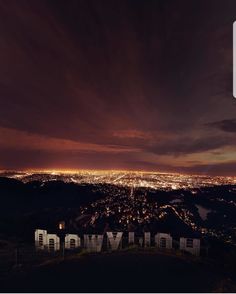 the hollywood sign is lit up at night with lights in the city below and dark clouds overhead