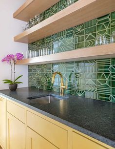 a kitchen with yellow cabinets and green tile backsplash, gold faucet